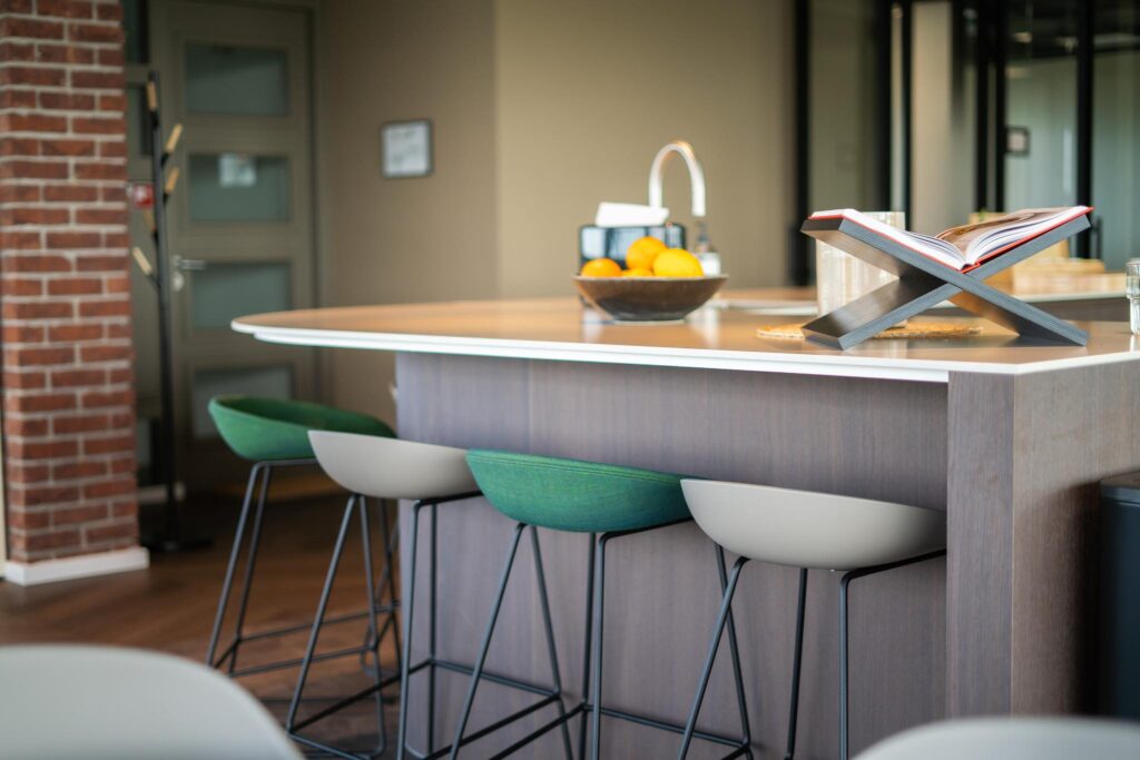 Modern kitchen island with bar stools, a fruit bowl, and an open book on a stand at Joop Geesinkweg.